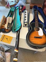 Overview of all instruments together on a table: guitar in case, violin in case, didjeridu, and keyboard melodica in case