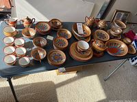 Layout of assorted tea cups, saucers, plates, bowls, sugar bowl and creamer displayed on folding table