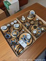 Full boxed lot of 1000 Faces china tea set parts in colorful black band design.