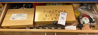 Drawer containing wooden boxes with Forstner bit set labelled 1/4"–2-1/8", and scattered router bits and hole saw components