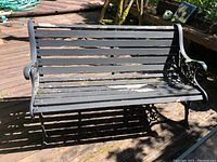 Photo showing front view of outdoor bench with wood slats and cast iron sides. Wood is weathered with flaking paint.