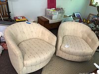 Two matching beige upholstered barrel-style chairs side by side in a room