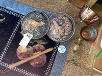 Two copper wall plates with embossed animal motifs and a copper coal scuttle with brass handle among other brass and copper items on a carpeted floor.