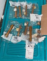 Top-down view of 11 wooden drawer pulls in individual plastic packaging arranged on a teal surface.