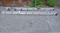 Full length view of folded 16-foot aluminum extension ladder with visible locking mechanisms and rubber end caps.