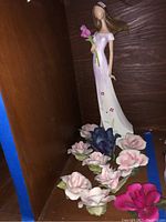 Photo of ceramic figurine with woman in long white dress holding a pink flower and ceramic flowers in front