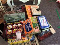 Photo of multiple boxed board games including Scrabble, Dominos, Fun With Lotto, Magic Mosaic, Journey Through Europe, Glass Chess Sets, Perplexus, and Sribbage packed together on floor.