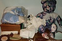 Floral fabric stuffed bear, knitted doll clothes in plastic bag, jewelry box, keepsakes and cloth fabric items displayed together