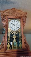 Full view of the mantel clock showing carved wooden case and decorative glass door with gold paint design