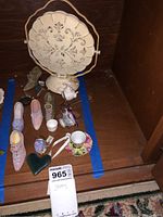 Photo showing assortment of miniature decorative shoes, tea cup, teapot, heart-shaped item, and round decorative piece on stand indoors on wooden surface.