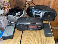 Photo of 3 portable radios and microphone/speaker device on wooden shelf showing front and side views.