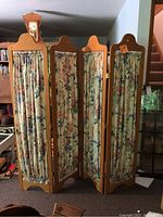 Front view of the four-panel wooden room divider with floral fabric panels and curved top edges.