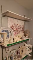 Shelf with white wicker mirror, various sea shells, candle holders, decorative vases and ceramic figurines arranged on two shelves.