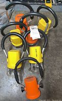 Six Trainman lanterns including five yellow and one orange with black handles on a concrete floor.
