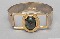 Oblique front view of brass bangle featuring large black oval stone centerpiece and showing detail of band and clasp.