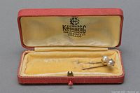 Two gold stick pins with pearls in a vintage red jewelry box with cream interior stamped 'Edward Kirchberg Diamonds Chicago'