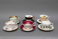 Front view of six bone china teacup and saucer sets arranged in two rows, showcasing patterns and gold trim.