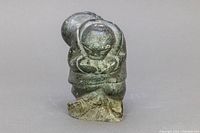 Front and slightly left angle view of the Inuit soapstone figurine showing rounded form and crouching posture with minor wear on surface and rough base.