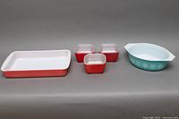 Full set of Mid-Century Modern Pyrex glassware displaying three small square refrigerator dishes with clear lids and two baking dishes, one rectangular in Pink Flamingo pattern and one round Snowflake pattern.