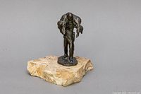 Front and side view of bronze sculpture of hunter carrying deer on stone base