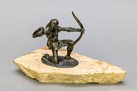 Front side showing Native American hunter figure kneeling with bow drawn on stone base.