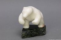 Front and side view of white stone bear sculpture on dark green stone base showing overall form and minor discoloration.
