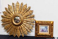 Full view of gold painted wooden sunburst mirror and gilt picture frame side by side