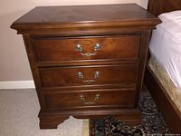 Front view of nightstand showing three drawers with metal handles and visible scratches on surface.