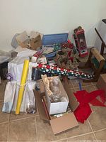 Overall view of wrapping paper rolls, boxes of Christmas decorations, wreath, and other holiday items on tiled floor