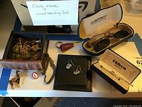 Full assortment of costume jewelry pieces including pins, earrings, bracelets, and eyeglasses with cases on a table