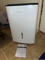 Full view of a white Frigidaire dehumidifier with the manual placed in front of it on the floor.