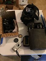 Various cameras, lenses, flash, and Sony Handycam on white table as displayed in seller's lot