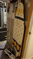 Photo of full size ironing board with celestial fabric cover hanging vertically, next to a wall and basement equipment.