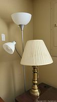 Photo showing the floor lamp with two white plastic shades and the brass table lamp with soiled cream pleated fabric shade on a table.