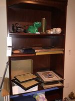 Photos show a wooden shelf with a green mesh bag containing marbles, several baseballs, softballs, a golf ball, and numerous picture frames stacked and arranged on the shelves.
