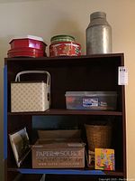 Shelf holding various art supplies, decorative cookie tins, large metal container, baskets, and framed photograph