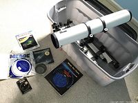 Photo showing the Meade Model 4500 telescope mounted on tripod legs inside a large plastic tote bin along with several star chart books and guides spread nearby on the floor.