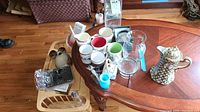 Lot overview on wooden table with mugs, vases, pitcher, figurine, lap desk, and scale