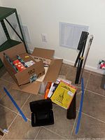 Lot arrangement showing boxes, music books, recorder, harmonica, bow, and tripod on tile floor.