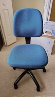 Frontal view of blue upholstered office chair with cushioned backrest and seat, showing swivel base and caster wheels.