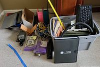 Overview photo showing various office supplies including electrical items, binders, cables, a keyboard, and organizing bins placed on carpet.