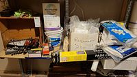 Photo showing assorted tools, buckets of grout, window film rolls, electrical part bags, and cleaning supplies arranged on metal shelving