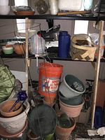 Shelf with assorted terracotta and plastic pots with a large orange bucket and wire tomato cage