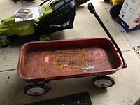 Full view of red Radio Flyer wagon with rust and dirt inside, black handle extended, white wheels with red centers visible.
