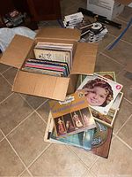Box with multiple vintage vinyl record albums inside and some laid out around the box including Shirley Temple and Guitars Galore albums