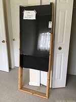 Full view of rectangular homemade solar panel with wooden frame and black plexiglass cover leaning against wall.