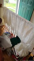 White lace tablecloth hanging over stair railing with other linens below