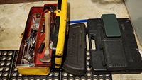 Open yellow metal toolbox showing assorted hand tools including hammers, screwdrivers, and wrenches inside top tray and bottom