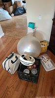 Photo showing silver yoga ball, rolled teal yoga mat, white and navy gym bag, black crate with dumbbells and bike helmet, bowling ball with bag, first aid kit box