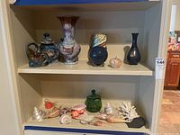 Full view of shelf with assorted vases, glass candy jar, shell decorations and figurines.